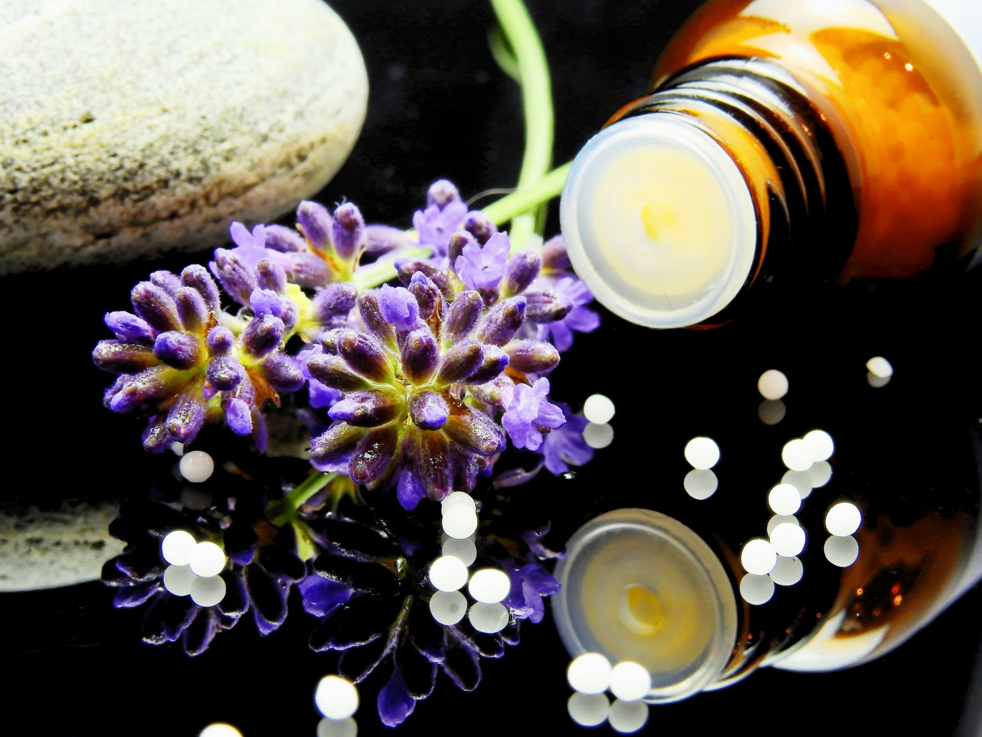 Lavendelblüten mit pflanzlicher Homöopathie auf reflektierender Oberfläche, ideal für Naturheilverfahren.