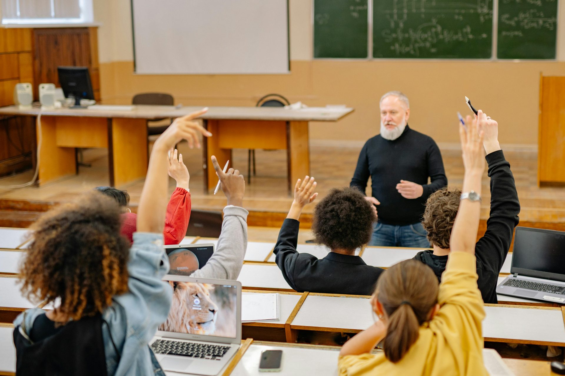 Die Studierenden beteiligen sich aktiv an einer Universitätsvorlesung, indem sie die Hand heben und über die Themen diskutieren.