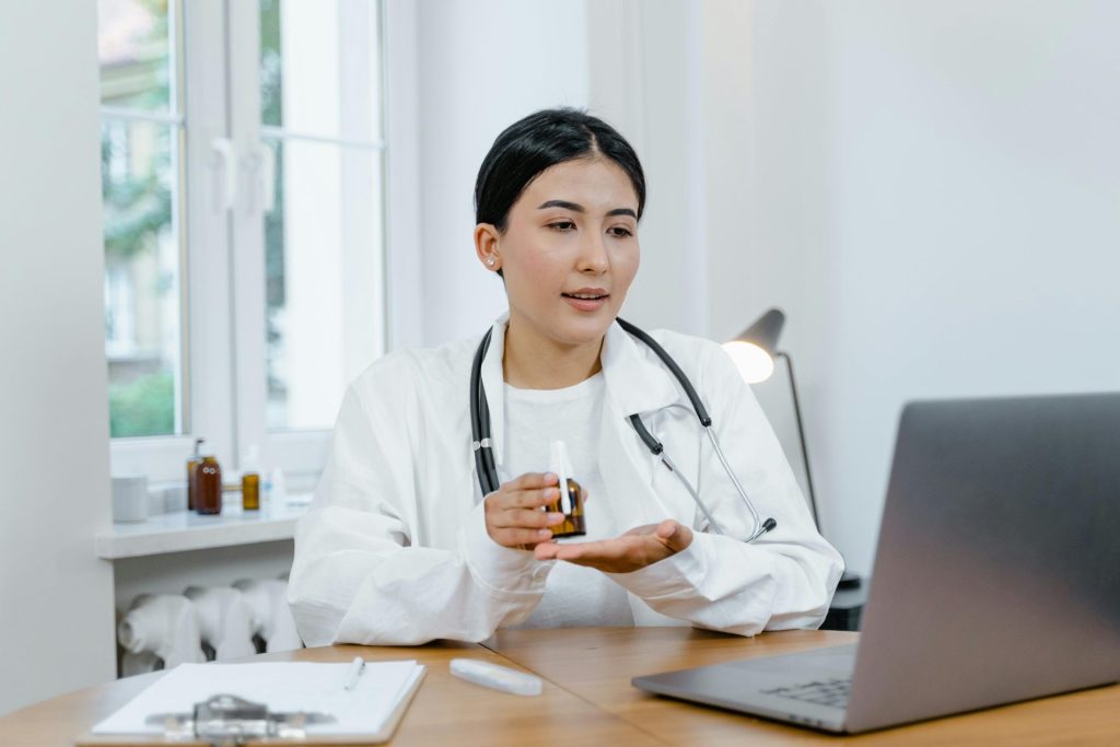 Eine junge Ärztin im weißen Kittel bespricht per Videoanruf mit einem Patienten Medikamente.